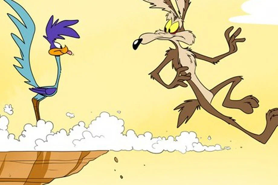 Coyote having run off of the cliff, looking backwards at roadrunner standing on the edge